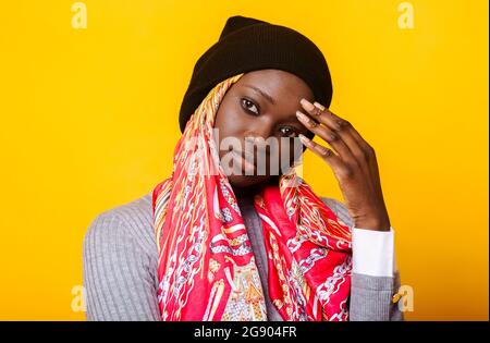 Schöne junge Frau im Kopftuch, die vor gelbem Hintergrund steht Stockfoto