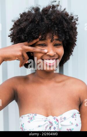 Lächelnde junge Frau, die vor der Wand eine Friedensgeste macht Stockfoto