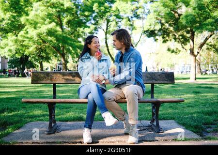 Lächelnde Schwangere, die einen Apfel hat, während sie den Ehemann im öffentlichen Park ansieht Stockfoto