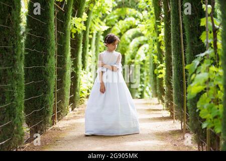 Mädchen im weißen Abendkleid, das im Garten steht und nach unten schaut Stockfoto