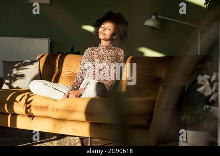 Entspannte Frau mit geschlossenen Augen sitzt auf dem Sofa im Wohnzimmer Stockfoto