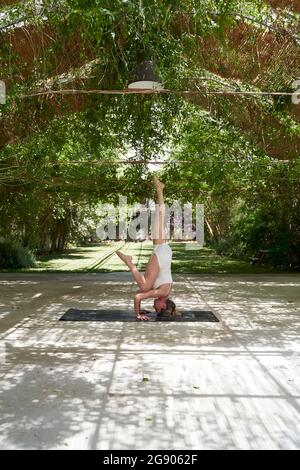 Reife Frau übt Kopfstand auf Yoga-Matte im Garten Stockfoto