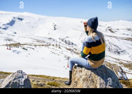 Junge Frau, die an sonnigen Tagen auf einem Felsen sitzt und die Augen abschirmt Stockfoto