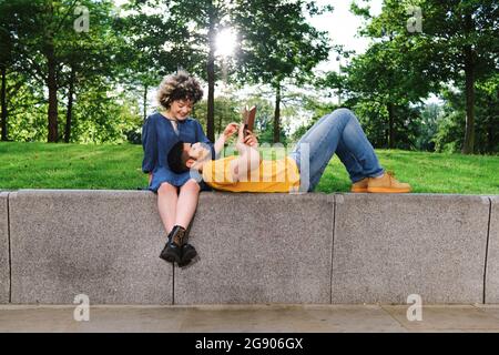 Freund liest Buch, während er auf dem Schoß seiner Freundin im Park liegt Stockfoto