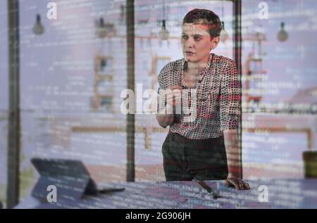 Nachdenkliche Geschäftsfrau, die sich neben dem Schreibtisch mit Binärcodes auf dem Glas lehnte Stockfoto