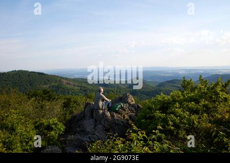 Männlicher Wanderer, der die Landschaft betrachtet, während er auf dem Berg sitzt Stockfoto