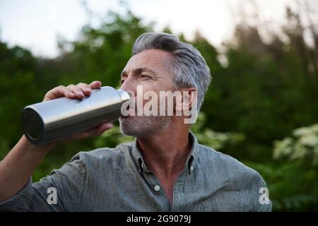 Männlicher Wanderer, der Wasser aus der Flasche im Wald trinkt Stockfoto