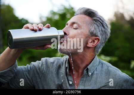 Durstiger Mann, der im Wald Wasser aus der Flasche trinkt Stockfoto