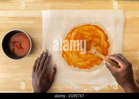 Mann, der Sauce verteilt, während er Pizza in der Küche macht Stockfoto