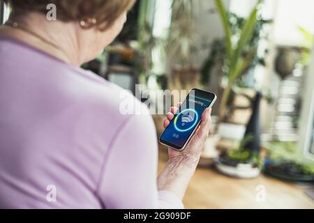 Ältere Frau, die zu Hause ein Mobiltelefon mit WLAN verbindet Stockfoto