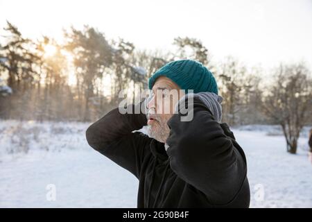 Älterer Mann mit Händen hinter dem Kopf, der im Winter Strickmütze trägt Stockfoto