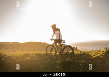 Reifer männlicher Athlet, der bei Sonnenuntergang Mountainbike fährt Stockfoto