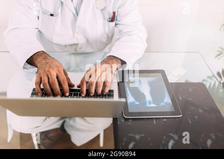 Leitender männlicher Arzt, der am Schreibtisch in der Klinik am Laptop arbeitet Stockfoto