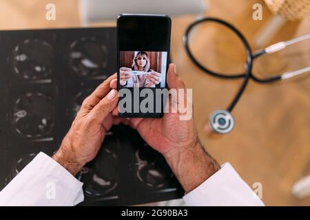 Weibliche Patientin, die dem Arzt während eines Videoanrufs in der Klinik ein Thermometer zeigt Stockfoto