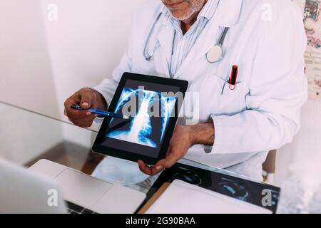 Leitender Arzt erklärt Röntgenaufnahmen auf einem digitalen Tablet im Krankenhaus Stockfoto