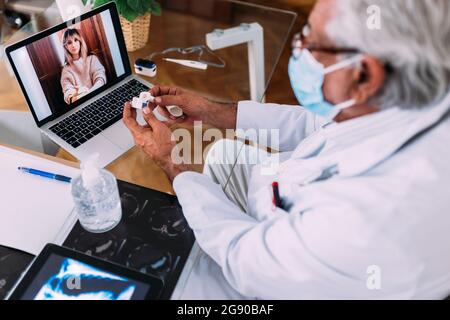 Männlicher Arzt, der während des COVID-19 eine schützende Gesichtsmaske trägt und weibliche Patienten in der Klinik unterstützt Stockfoto