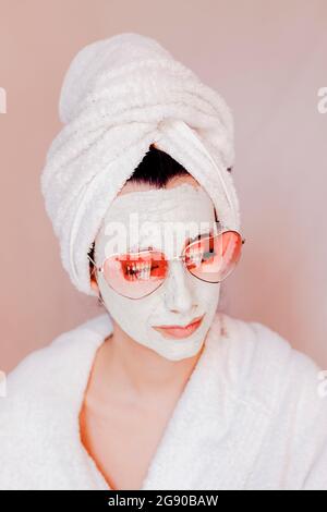 Junge Frau mit Beauty-Gesichtsmaske trägt herzförmige Sonnenbrille Stockfoto