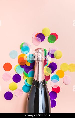 Studioaufnahme einer Flasche Champagner und farbenfroher Konfetti vor pastellrosa Hintergrund Stockfoto