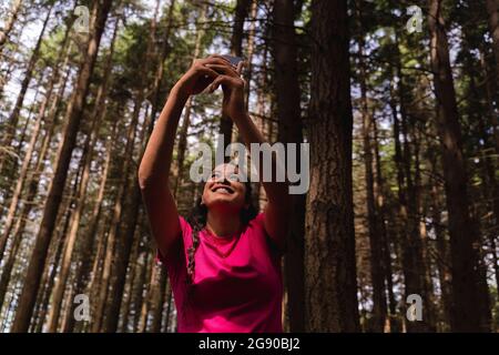 Lächelnde Wandererin, die Selfie durch das Mobiltelefon mit Bäumen im Hintergrund beim Wald gemacht hat Stockfoto