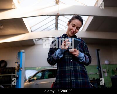 Weibliche Mechaniker mit Handy in Werkstatt Stockfoto