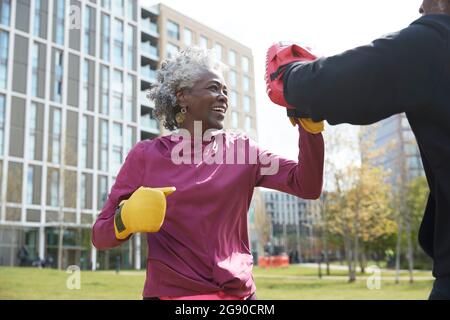 Lächelnde Frau, die am sonnigen Tag mit dem Mann im Park Boxen praktiziert Stockfoto