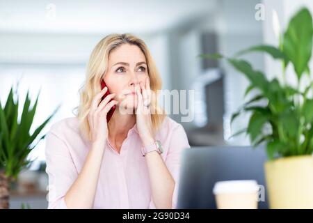 Erwägen Sie eine Geschäftsfrau, die im Heimbüro auf einem Smartphone spricht Stockfoto