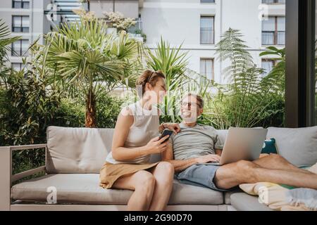 Lächelnde Frau, die mit dem Mann spricht, während sie auf dem Sofa sitzt Stockfoto