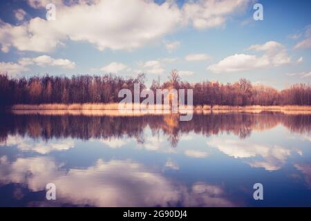 Friedlicher Blick auf einen kleinen See. Wald auf der anderen Seite eines Teiches. Wald und Wolken spiegeln sich auf der Wasseroberfläche. Chorzów, Schlesien, Polen Stockfoto