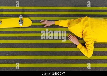 Junge greift nach Skateboard, während er auf gelben Straßenmarkierungen liegt Stockfoto