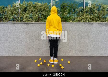 Junge inmitten von Zitronen und Gummiente, die vor einer Stützmauer stehen Stockfoto