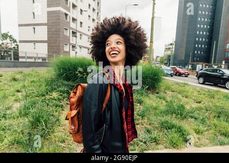 Glückliche Frau mit Rucksack, die in der Stadt über die Schulter blickt Stockfoto