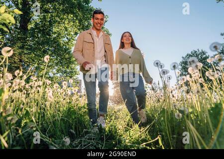 Glückliches junges Paar, das die Hände hält, während es inmitten von Blumen zusammenläuft Stockfoto