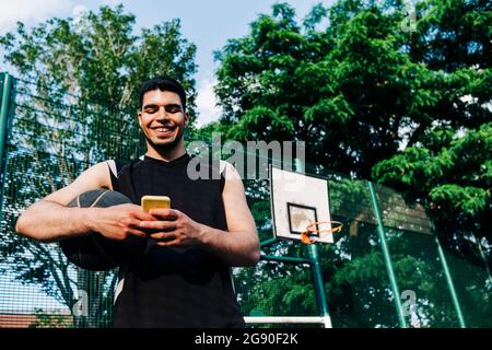 Lächelnder Sportler mit Smartphone auf dem Sportplatz Stockfoto