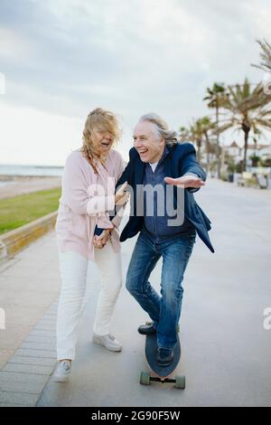 Reifer Mann genießt Skateboarding von Frau zu Fuß, während die Hände halten Stockfoto