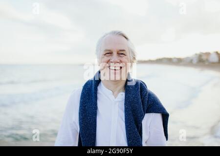 Glücklicher reifer Mann mit weißen Haaren an der Küste während des Urlaubs Stockfoto