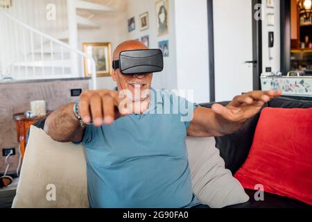 Mann, der zu Hause mit einer Virtual Reality Brille gestikelt hat Stockfoto