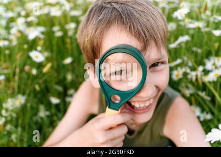 Fröhlicher Junge, der durch die Lupe ins Feld schaut Stockfoto