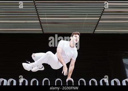 Junger Mann schaut weg, während er über Geländer springt Stockfoto