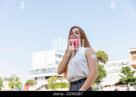 Schöne Geschäftsfrau, die wegschaut, während sie während einer Pandemie eine schützende Gesichtsmaske entfernt Stockfoto