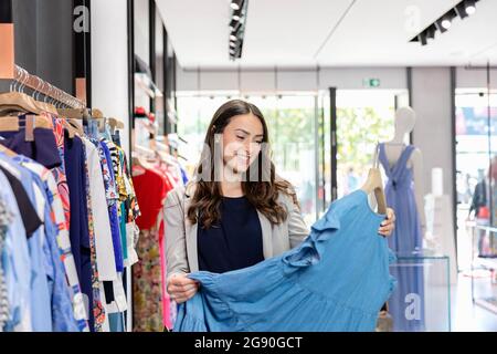 Lächelnde junge Frau mit blauem Kleid beim Einkaufen in der Boutique Stockfoto