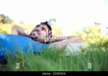 Junger Mann kontempliert, während er im Park auf Gras liegt Stockfoto