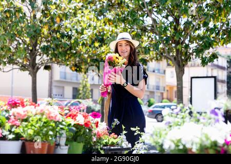Frau mit Sonnenhut hält Blumenstrauß im Blumenladen Stockfoto