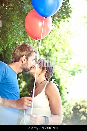 Junge Frau und Mann Ballons küssen im Park Stockfoto