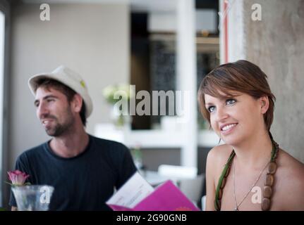 Junge Frau mit Menü, während sie von einem Freund im Restaurant sitzt Stockfoto
