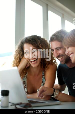 Glückliche Freunde und Freundinnen, die ihren Laptop im Restaurant teilen Stockfoto
