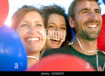 Glückliche männliche und weibliche Freunde inmitten von roten und blauen Ballons Stockfoto