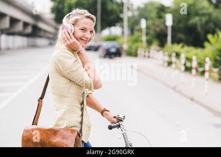 Fröhliche Pendlerin, die über Kopfhörer Musik hört, während sie mit dem Fahrrad unterwegs ist Stockfoto