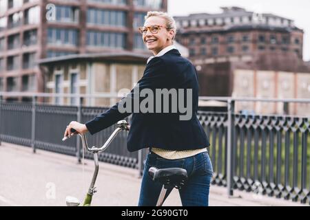 Glückliche weibliche Profi zu Fuß mit dem Fahrrad auf der Brücke Stockfoto
