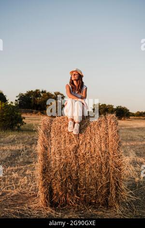 Frau mit geschlossenen Augen sitzt auf Strohballen auf dem Bauernhof Stockfoto