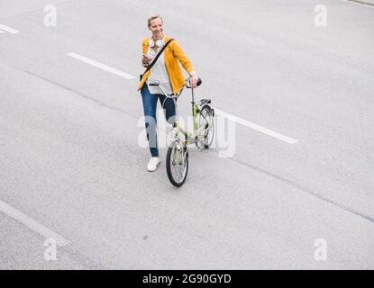 Lächelnde Frau, die mit dem Fahrrad auf der Straße läuft Stockfoto